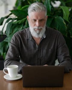 an attractive European man with a stylish haircut, with gray hair and a beard works at a laptop