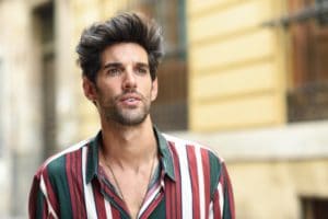 Attractive young man with dark hair and modern hairstyle wearing casual clothes outdoors