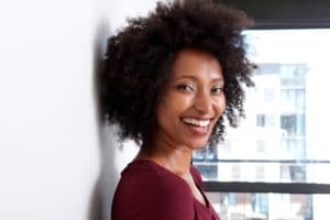 Close up african woman with curly hair leaning to wall at home and smiling
