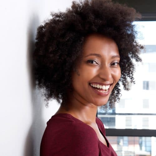 Close up african woman with curly hair leaning to wall at home and smiling