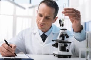 Concentrated lab technician taking notes while examining sample of plant in test tube