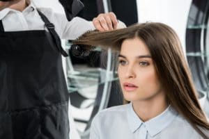 hairdresser brushing hair of beautiful young woman in beauty salon