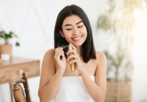 Pretty smiling asian woman applying hair oil at home